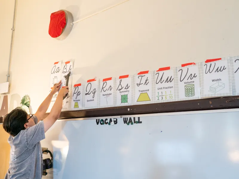 A young male student adding a piece of paper to the vocabulary wall.