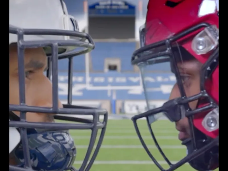 A screenshot of two players, one from Yale (left) and one from Harvard (right) with their helmets on facing each other.