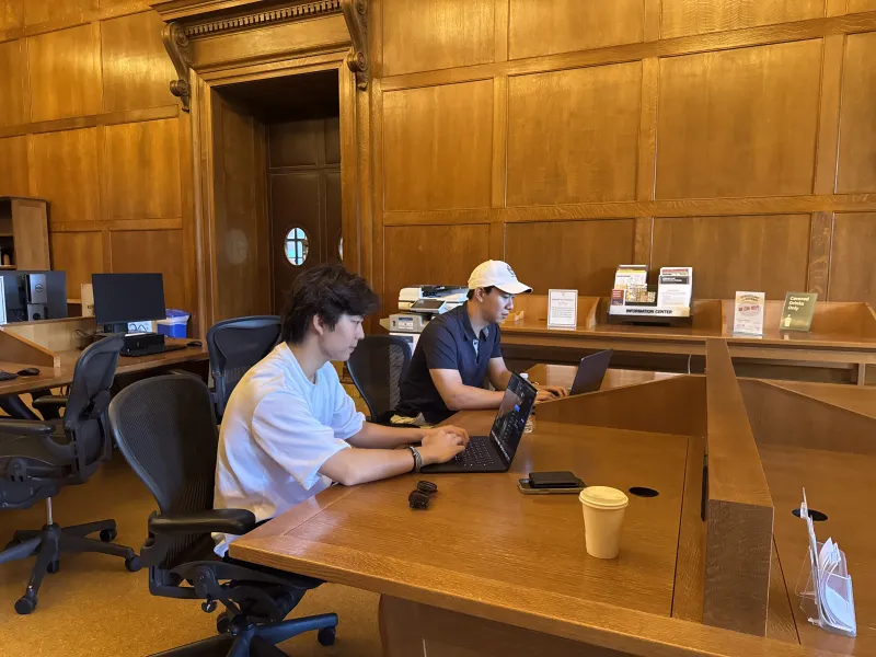 Two male students in 2026 seated at a table and working on their portable laptops.
