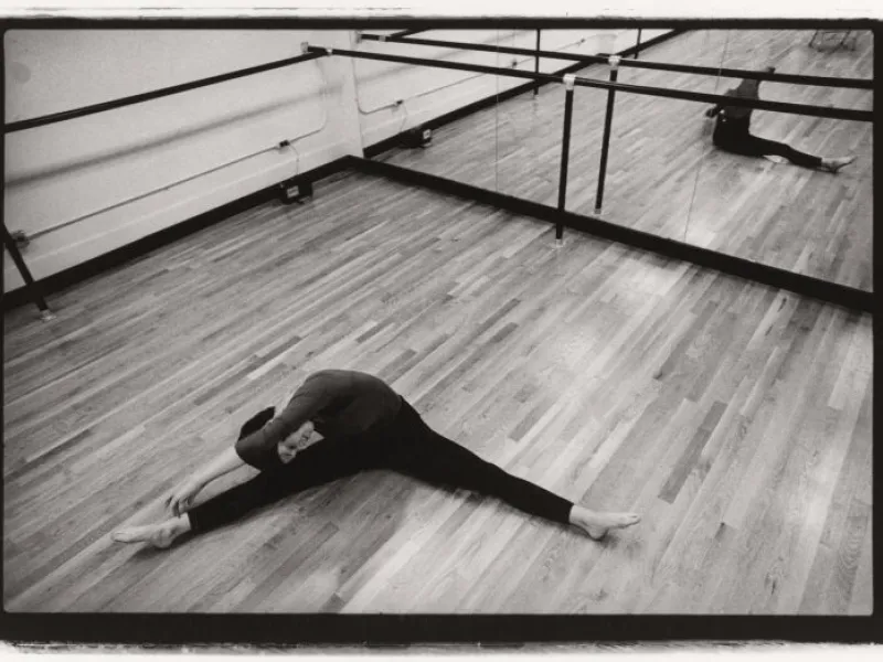 A black and white image of dancer Susan Manning stretching on the floor of Eliot House studio in 1977.