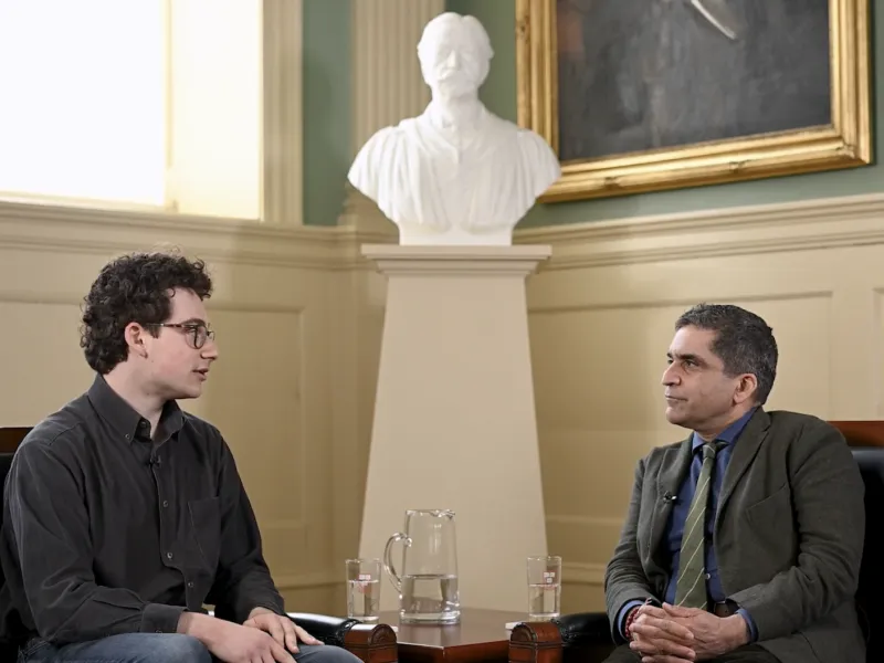 A male student (left) sitting next to Dean Rakesh Khurana (right) and talking.