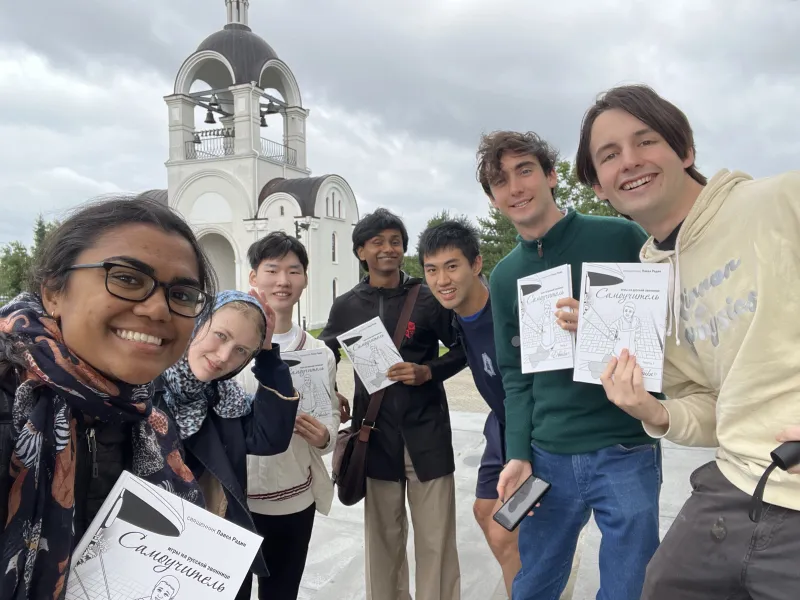 Seven students holding up white pamphlets about bellringing in front of a church in Estonia.