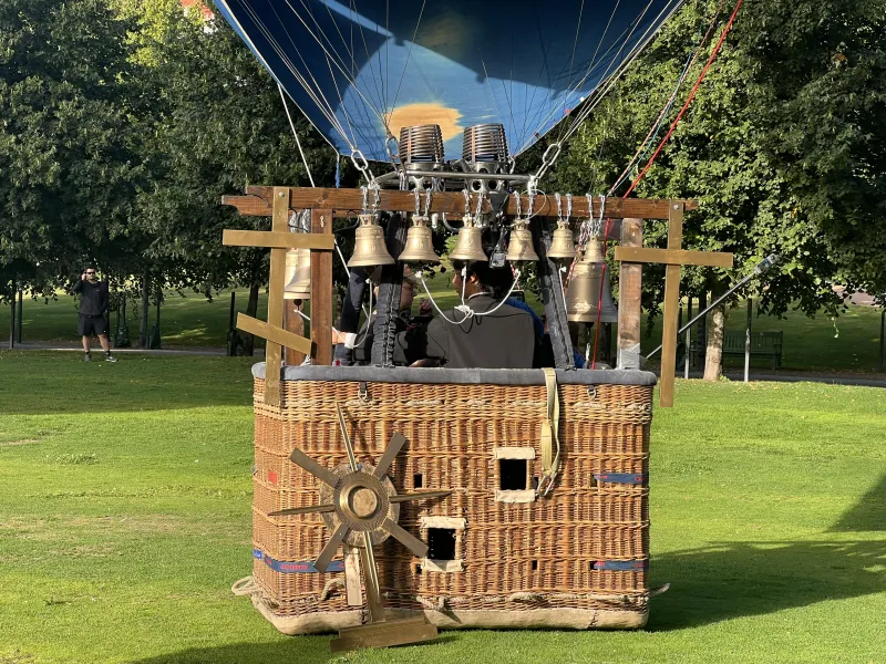 A student inside of a hot air balloon while still on the ground, with bells surrounding the balloon.