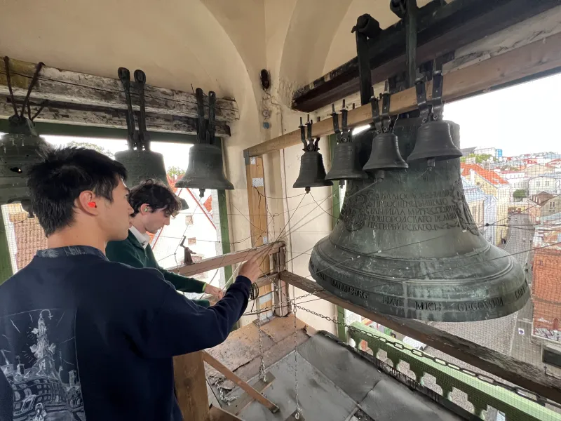 Two students standing inside the top of the belltower, pulling on some strings.