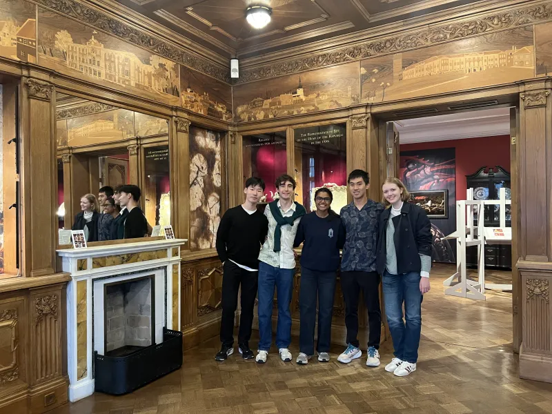 Five students huddled together for a picture inside of a museum with gold walls.