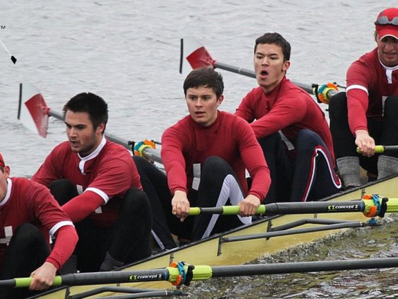 Students in crimson colored shirts rowing a boat