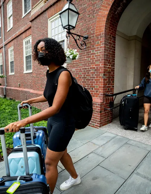 Halima Badri ’23 (left) and Maria Gonzalez ’23 enter the Lowell House courtyard with their luggage.