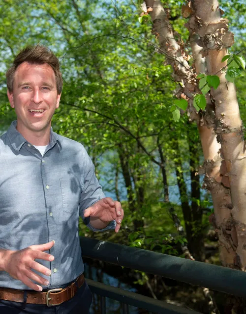 Jeffrey Wilson smiles next to a tree and in front of a water body
