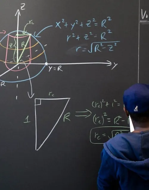 Hakim Walker, preceptor of mathematics, uses the chalkboard in the Science Center math lounge to try to solve a problem: finding the volume of a ball with a 2-centimeter-long cylindrical hole drilled through it.