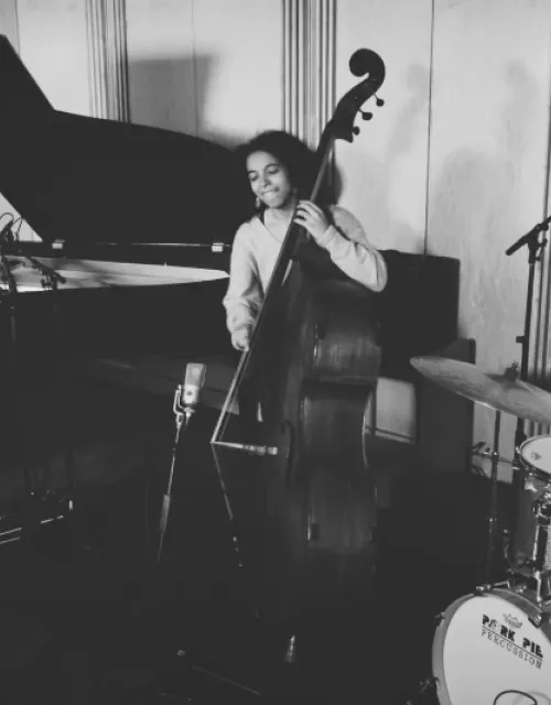 A black and white picture of a pianist playing the piano on the left, a bassist playing the bass in the middle, and a drummer playing the drums on the right.