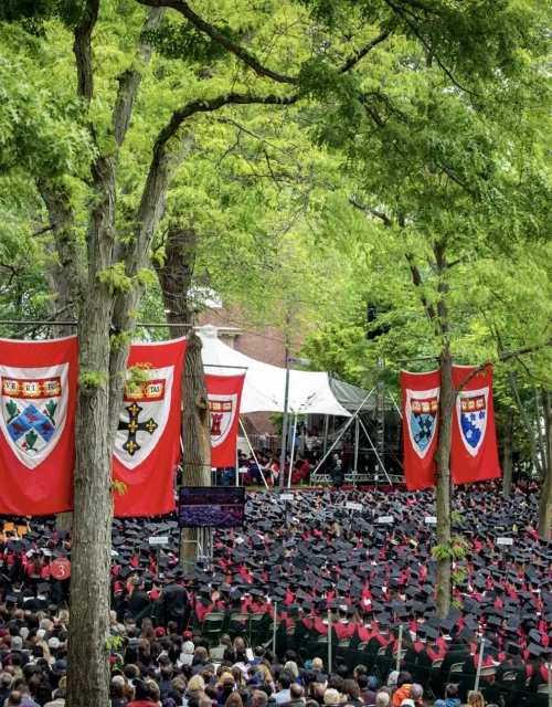 Students sitting in Harvard Yard for Class Day/Commencement with large Harvard banners