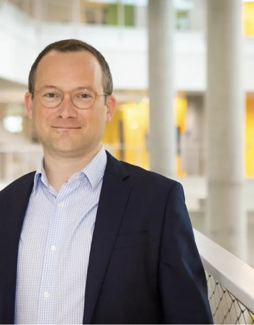 New SEAS Dean David Parkes smiles at the camera with the first floor of the Science and Engineering Complex (SEC) in the background.