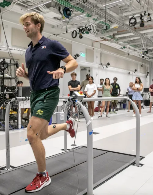 A man running on a treadmill with wires attached to his legs. 