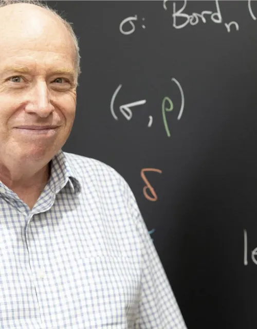 Professor Dan Freed standing in front of a chalk board covered in math symbols and equations.