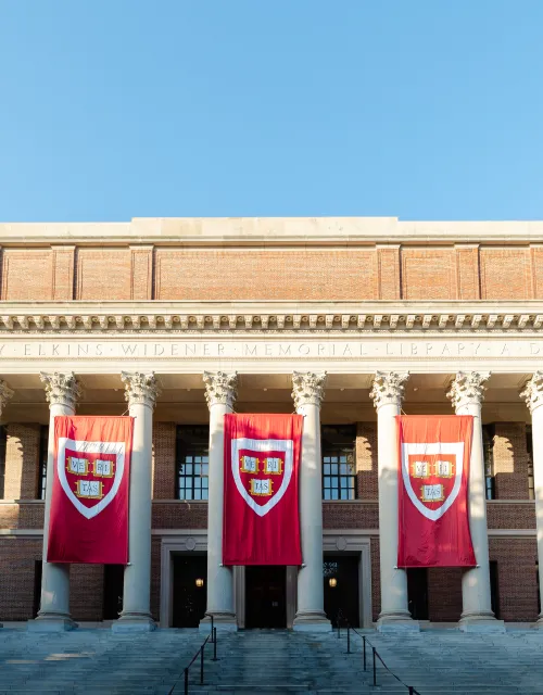 The facade of Widener Library with Harvard flags hung across its columns. 