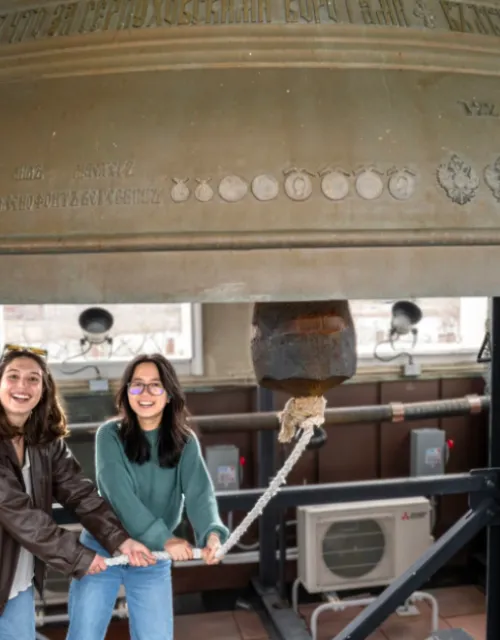 Sofia Giannuzzi (left) and Linh Vu ring a large bell in the Lowell House bell tower as part of a Sunday House tradition.