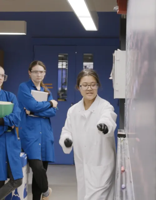 students in a lab with a professor. they are all wearing lab coats