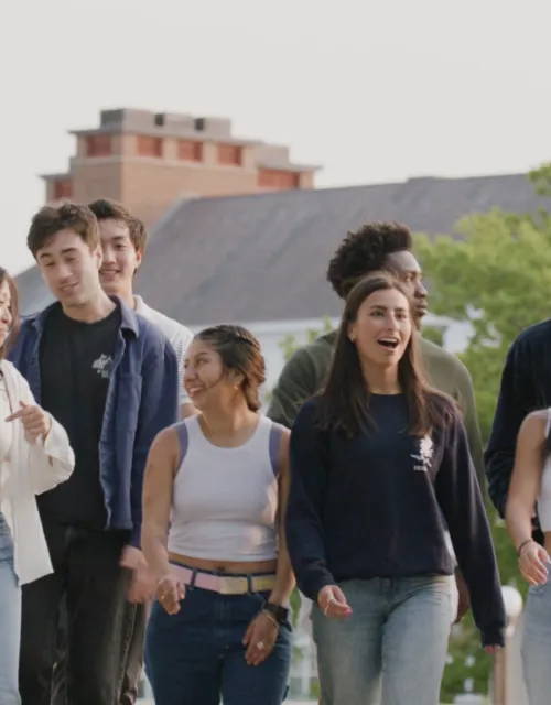group of students laughing and talking while walking over a bridge over the Charles River