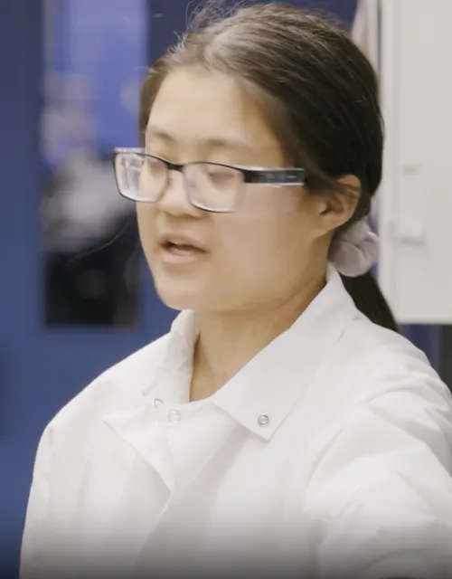 Student in lab coat and goggles at a white board