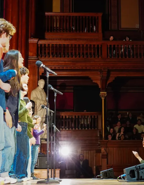 Performers on stage with microphones, while an audience watches.