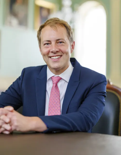 David Deming smiling while sitting at a table in a formal room.