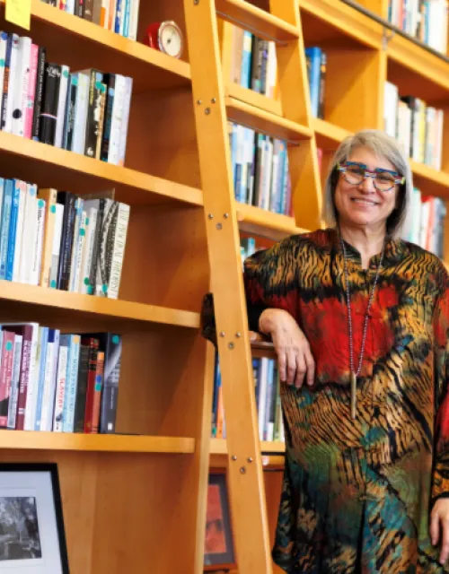 Banaji is standing and smiling in front of a large wall of books.