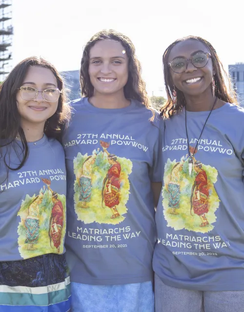 Three Harvard College students smile together while wearing Powwow 2025 t-shirts.