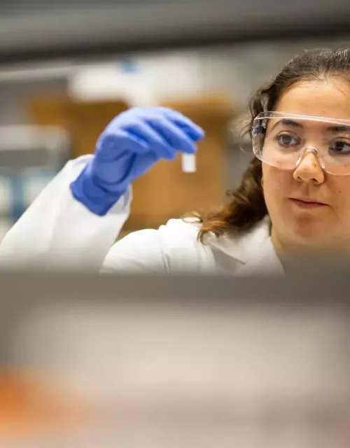 Olivia Hogan-Lopez in gloves and lab attire, looking at small test tube