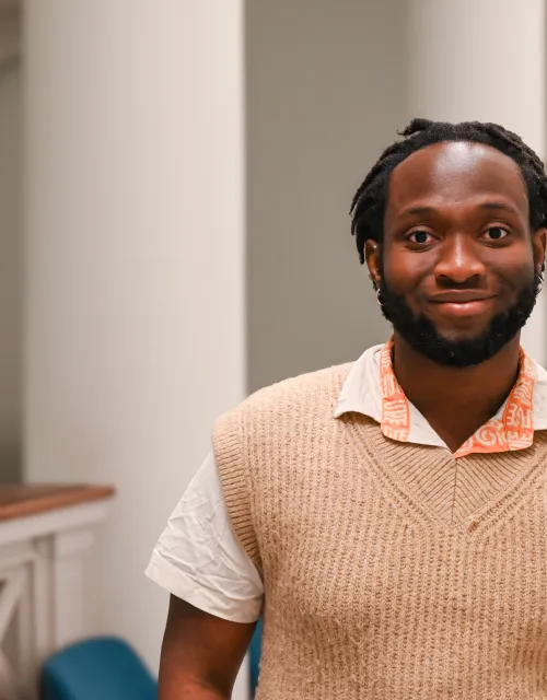 Hassan smiles while standing in a classroom hallway.