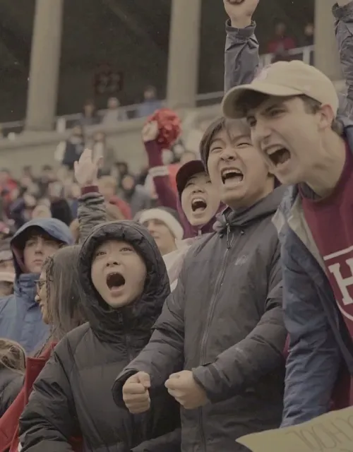 Excited crowd of Harvard fans cheer at a stadium event.
