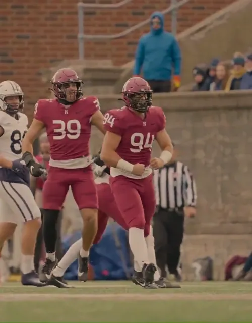 Harvard and Yale football players stand on the field as a referee signals during a game.