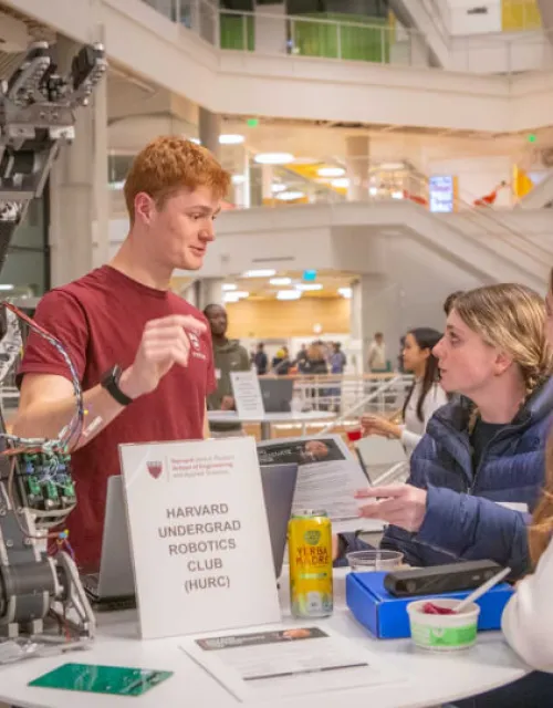 Two female students second-year students learn about the Harvard Undergraduate Robotics Club at Convocation.
