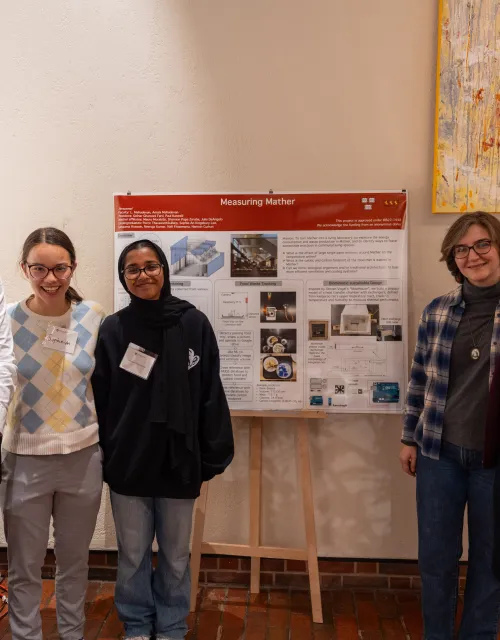 The Measure Mather team smile for a photo together next to a posterboard explaining their project.