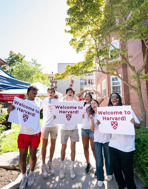 A group of Harvard College students cheer while holding up signs to welcome the incoming class.