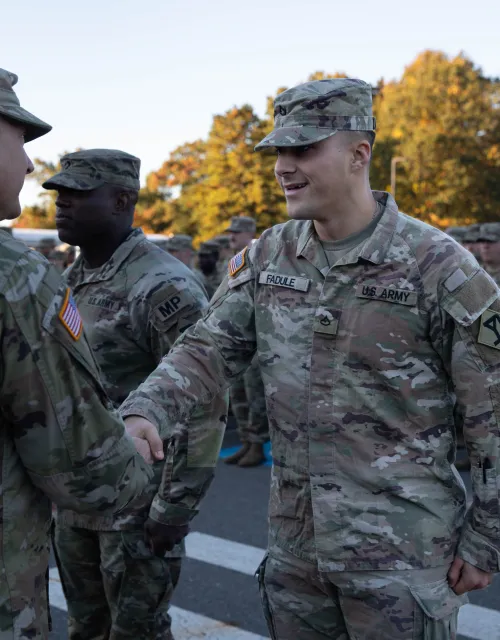 Dressed in his camoflauge uniform, Fadule smiles and shakes the hand of a fellow serviceman as he receives an award. 