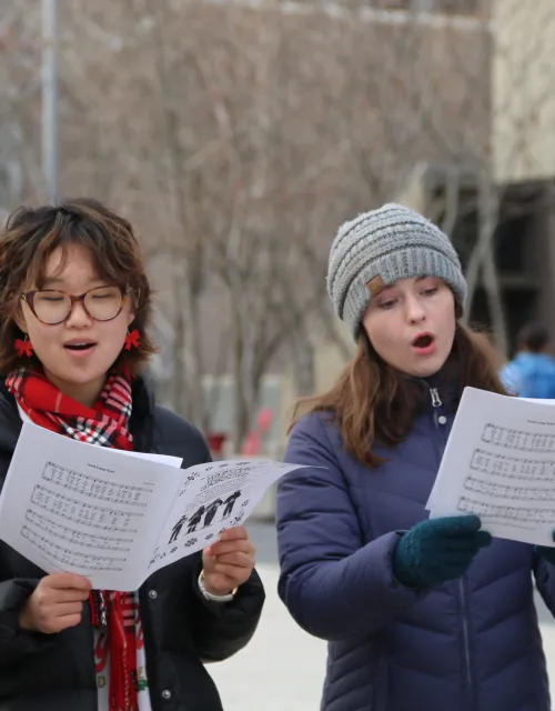Two female students read sheet music while singing outside on the Harvard campus.