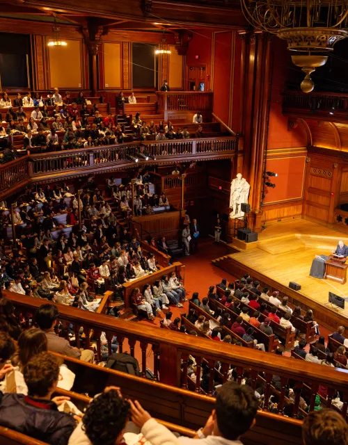 Interior of Sanders Theatre featuring two men on stage with full balconies
