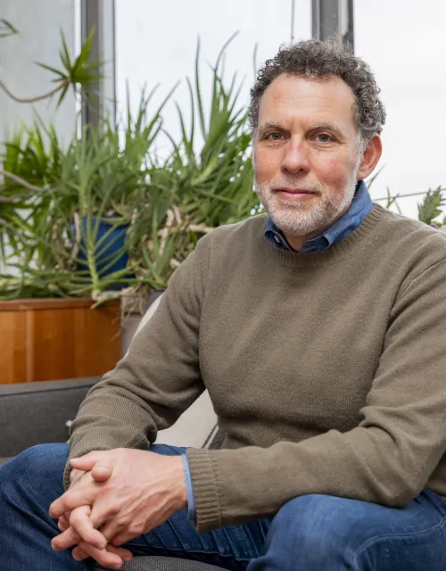 Joshua D. Greene sitting on a couch and staring intently at the camera.