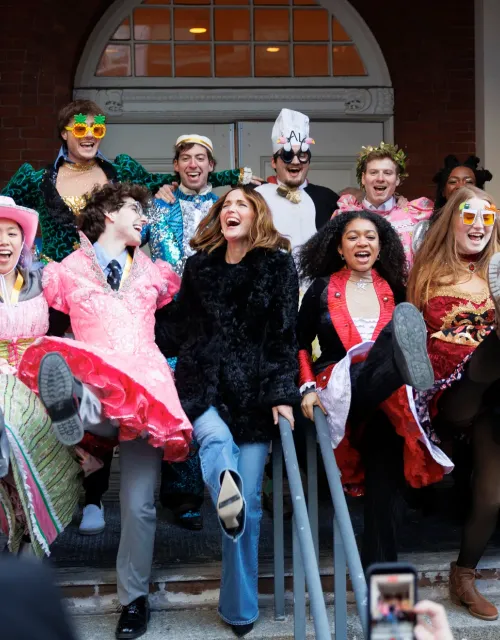 Group of people in colorful costumes laughing and kicking up their legs on steps.