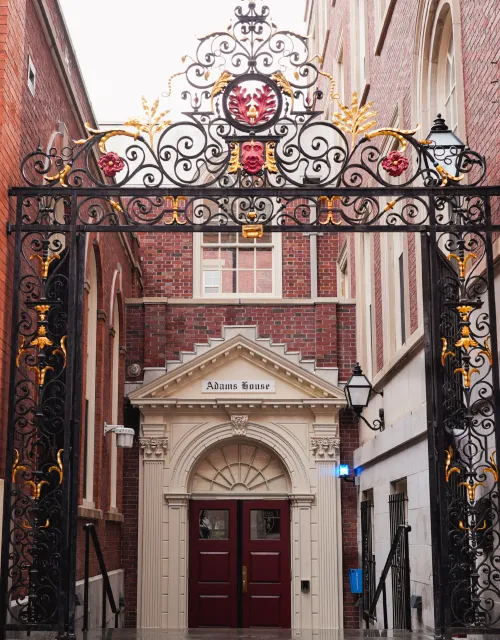  Ornate black and gold wrought-iron gate frames the red double-door entrance to Adams House.