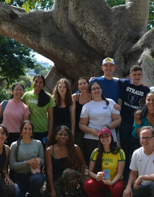 The group of students and two leaders posing together outside next to a large tree.