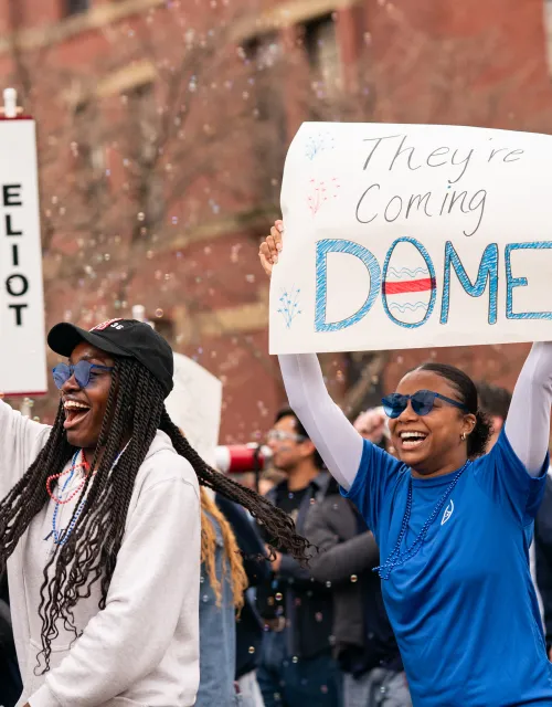 Students holding up a sign for Eliot House that reads "they're coming dome".