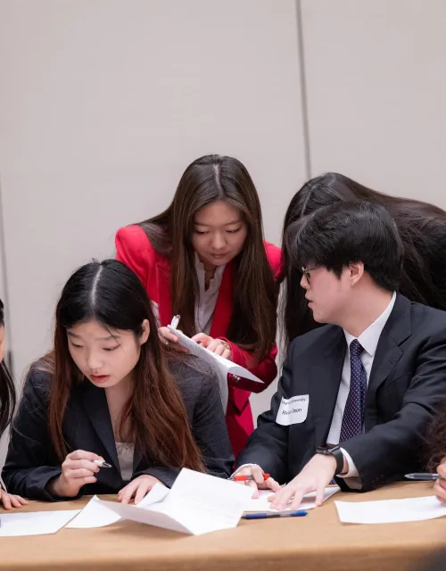 A group of students crowded around a desk and looking through papers.