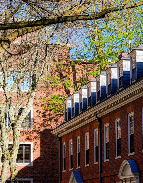 A close-up view of a historic red brick dormitory with slate-shingled dormer windows.
