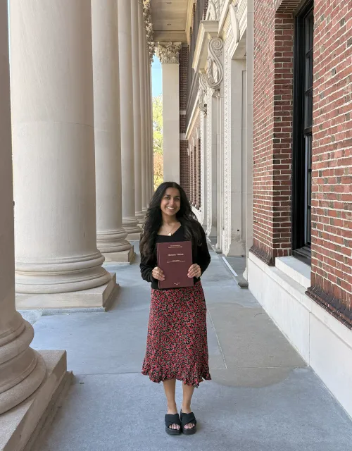 Gauri Sood '26 standing with her thesis papers in her hands.