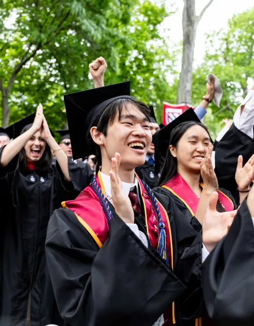 Students cheering in the crowd while wearing their regalia at Commencement.