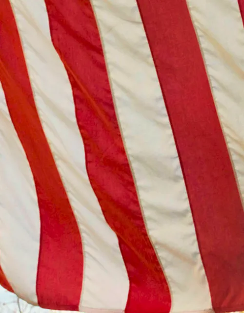 Close-up of an American flag’s red and white stripes above a bronze seated statue.