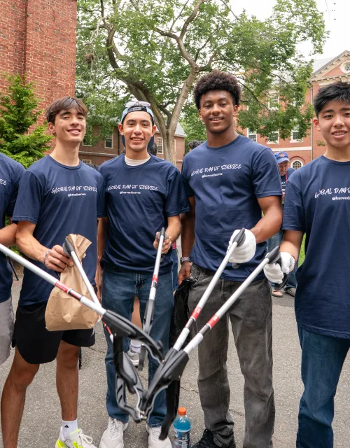 A group of 5 male students holding items to pick up trash.