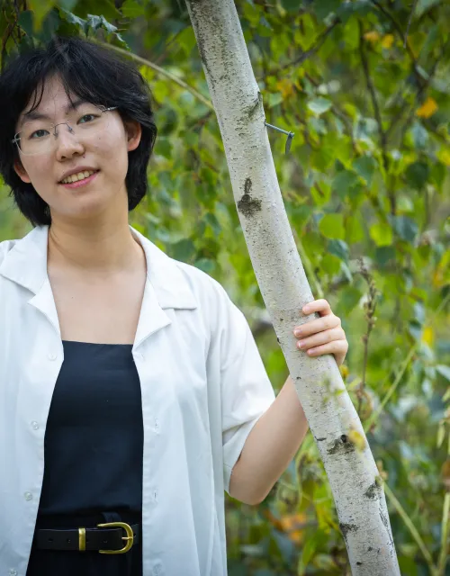 Luna Yin '28 standing outdoors holding onto tree bark and smiling.