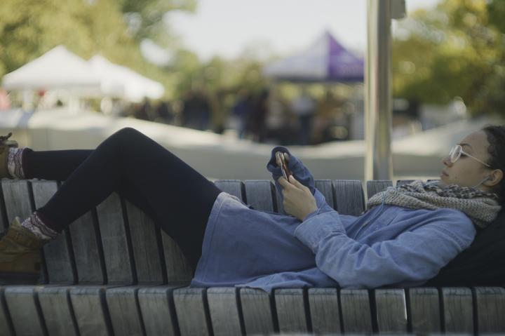 Student laying on bench at Science Center Plaza with her phone